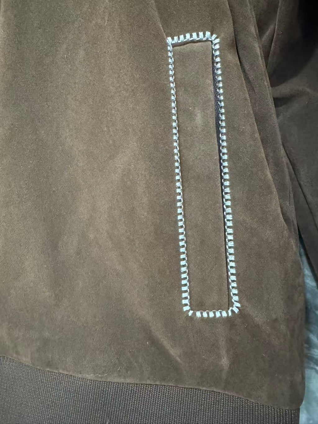 Brown jacket detail: rectangular flap pocket with white braided trim