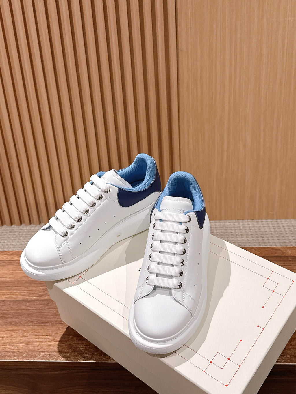 White leather sneakers with blue collar detail, side view on white box