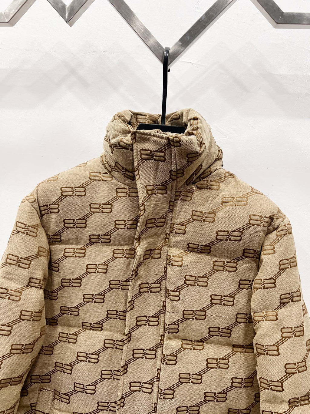 Balenciaga hooded puffer jacket close-up in beige with repeating logo pattern and front zip