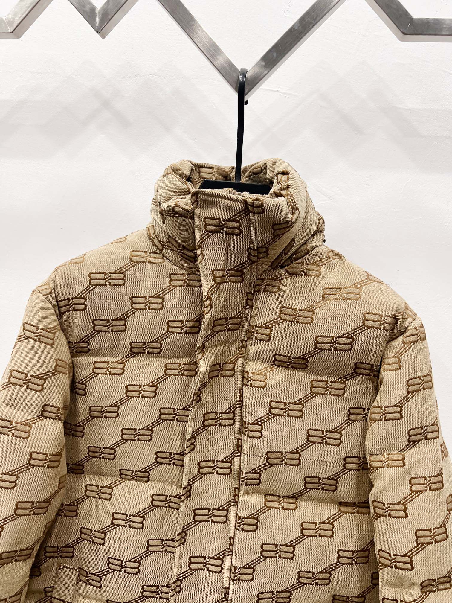 Balenciaga hooded puffer jacket close-up in beige with repeating logo pattern and front zip
