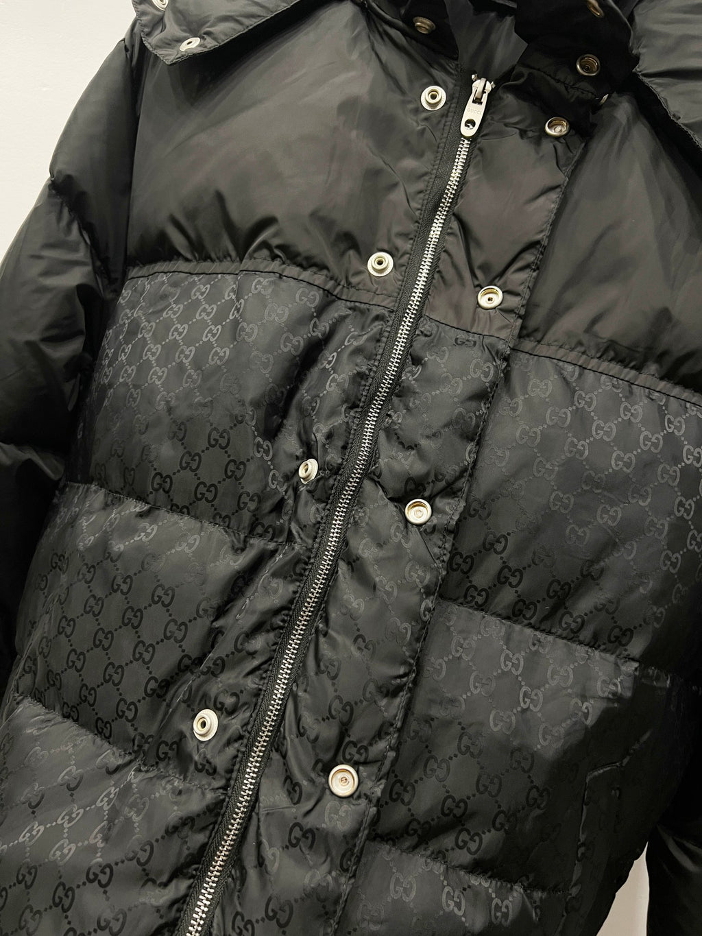 Dark puffer jacket front with zipper, snap buttons, and monogram pattern