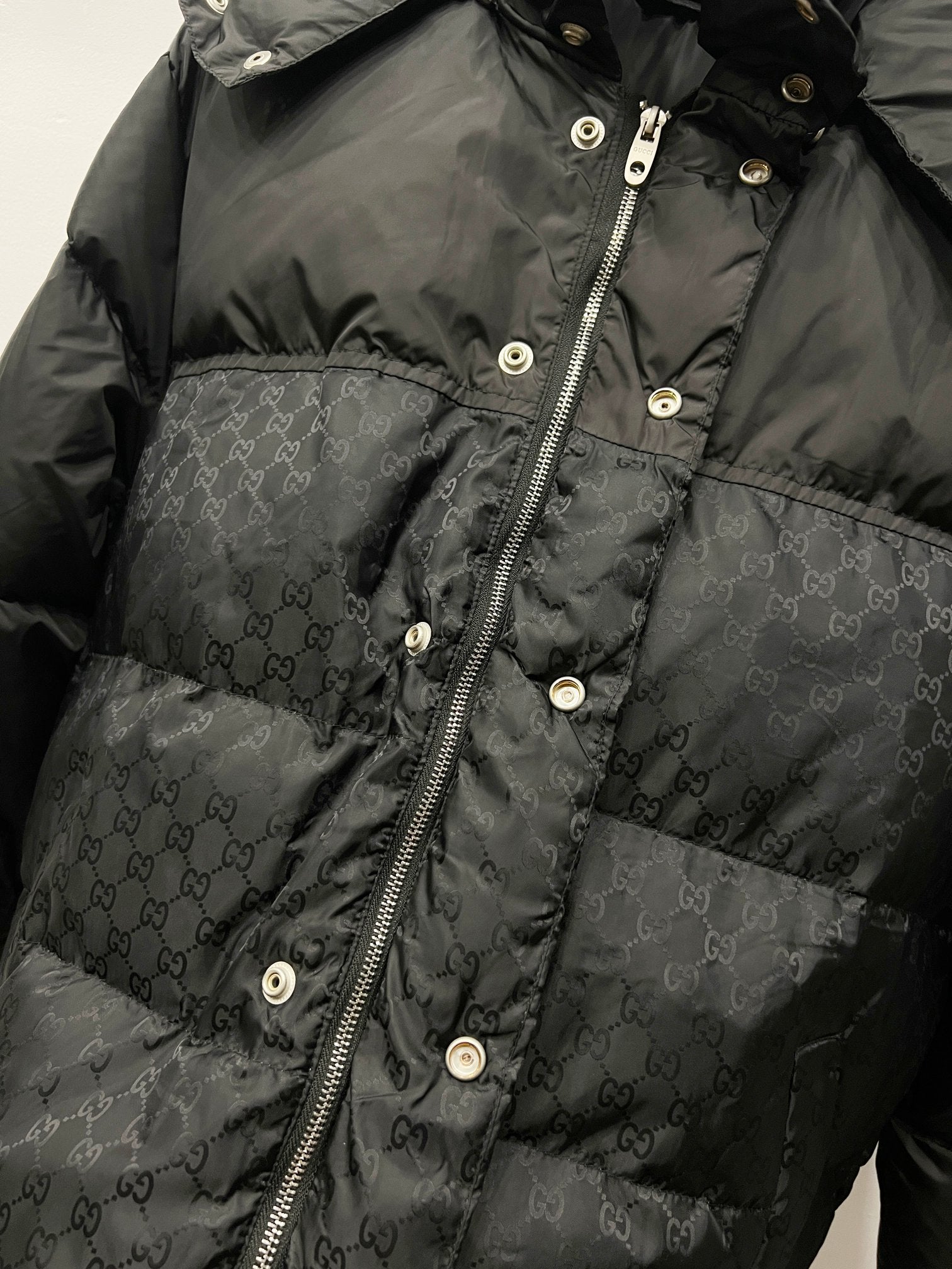 Dark puffer jacket front with zipper, snap buttons, and monogram pattern
