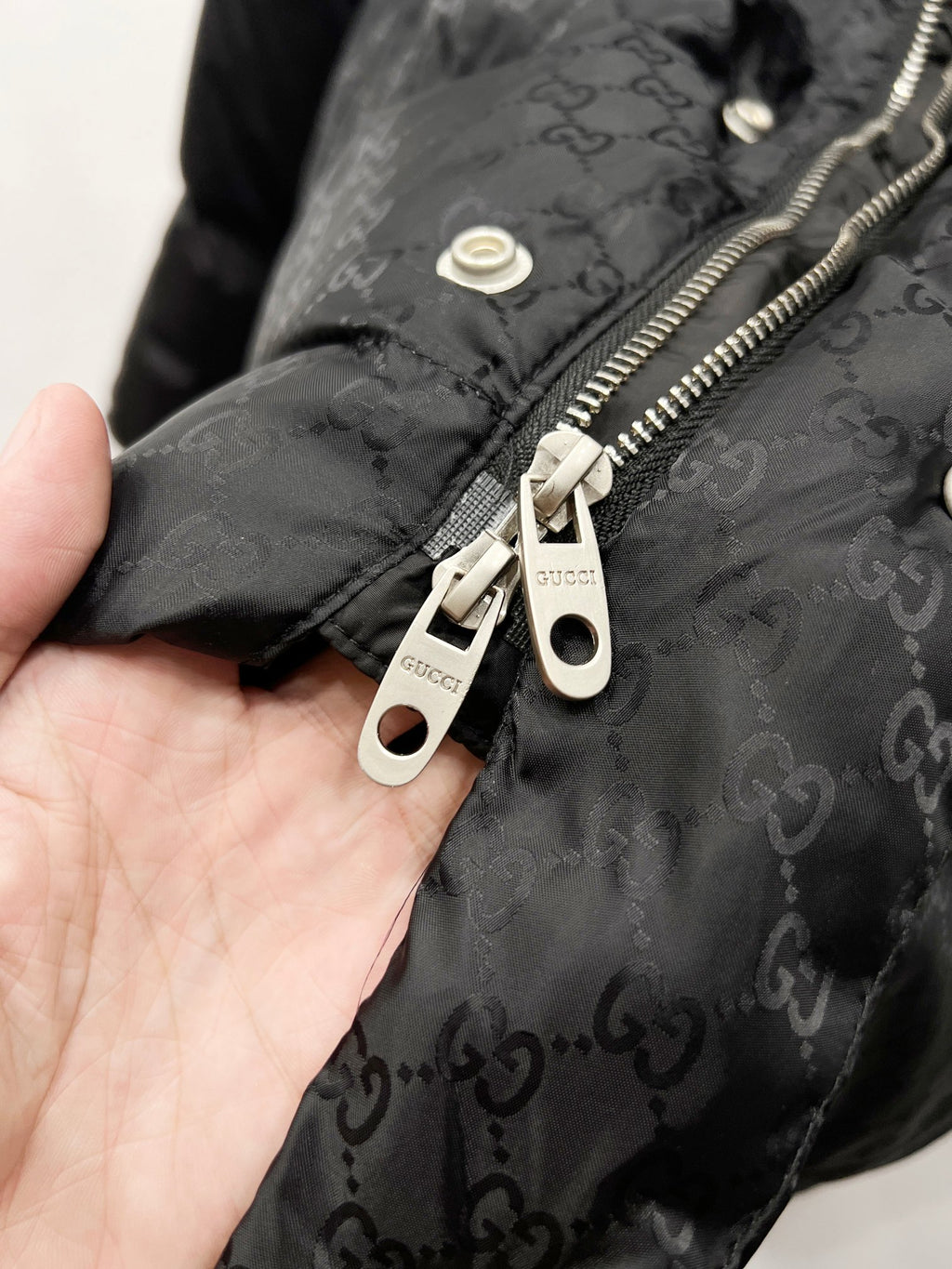 Dark puffer jacket detail: zipper pull and snap placket with Gucci tags