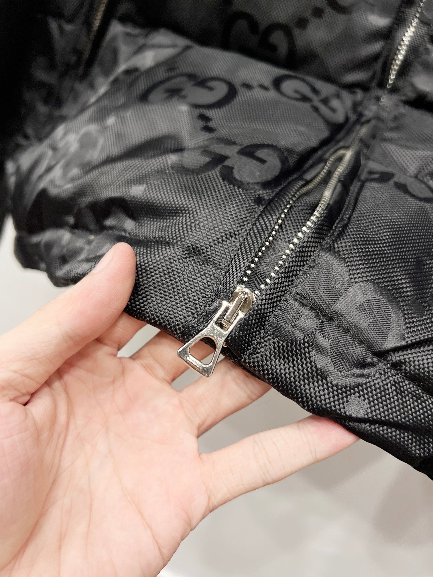 Gucci puffer jacket front zipper pull on dark GG-patterned fabric