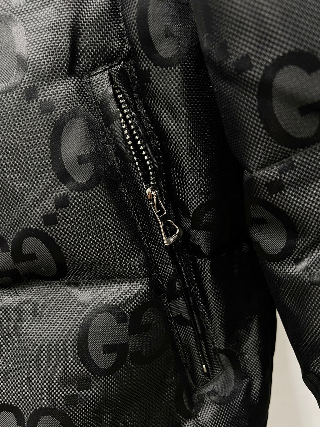 Gucci puffer jacket zipper pocket area with GG pattern on dark fabric