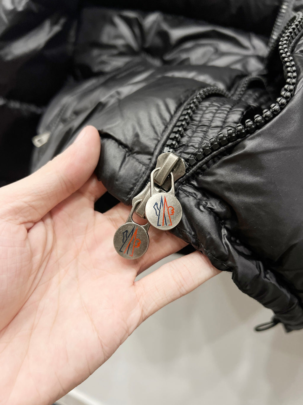 Moncler puffer jacket close-up, dark black zipper pull with logo tag