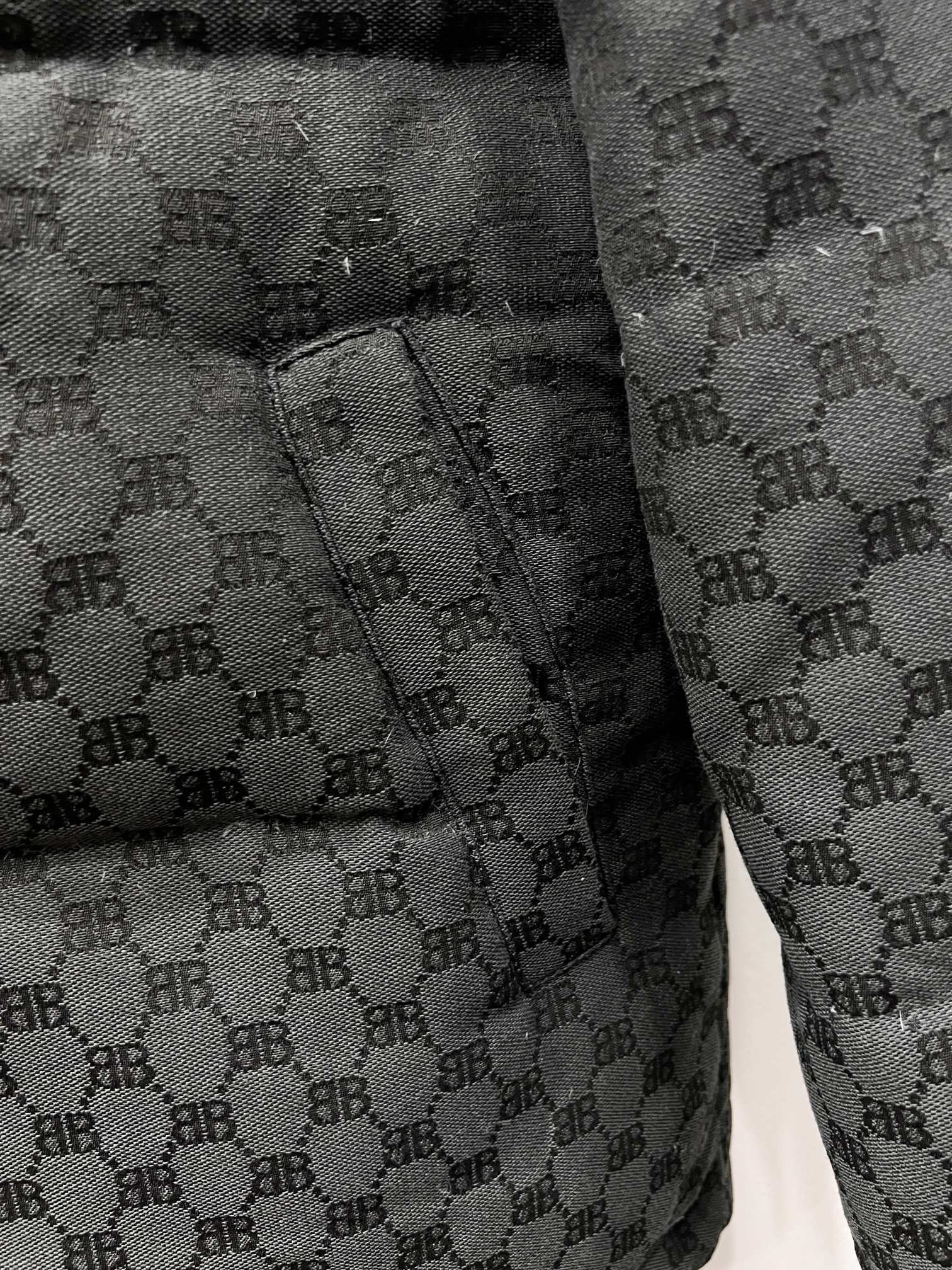 Dark gray puffer jacket sleeve cuff with quilted monogram fabric and stitched seam
