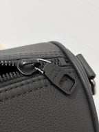 Louis Vuitton leather bag close-up with metal charm and zipper pull, dark gray.