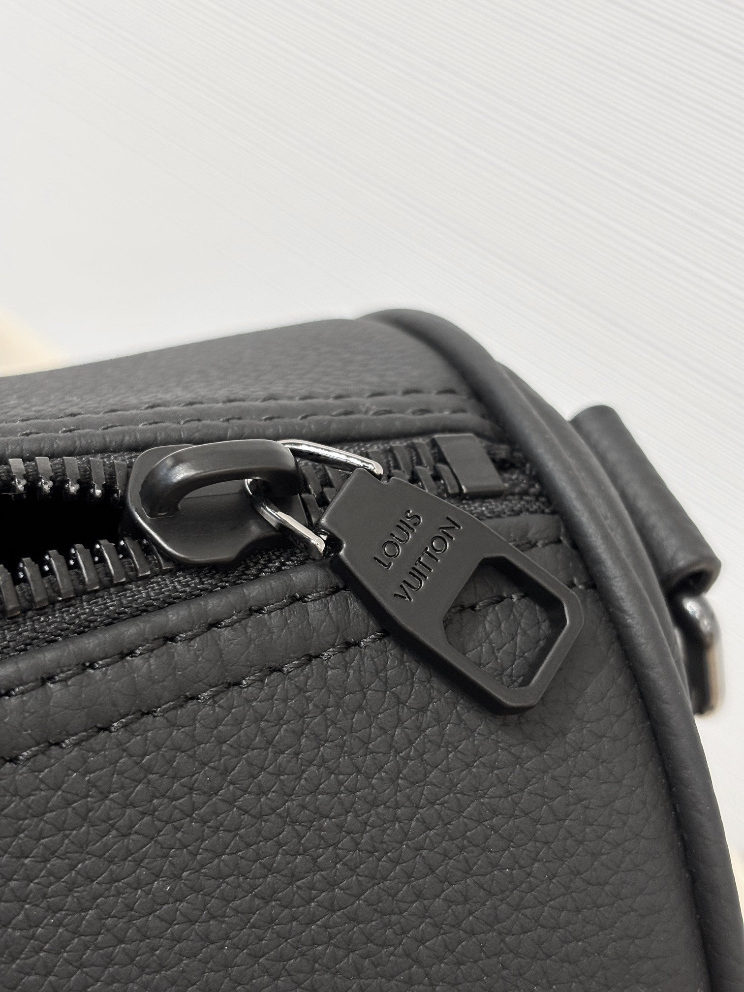 Louis Vuitton leather bag close-up with metal charm and zipper pull, dark gray.