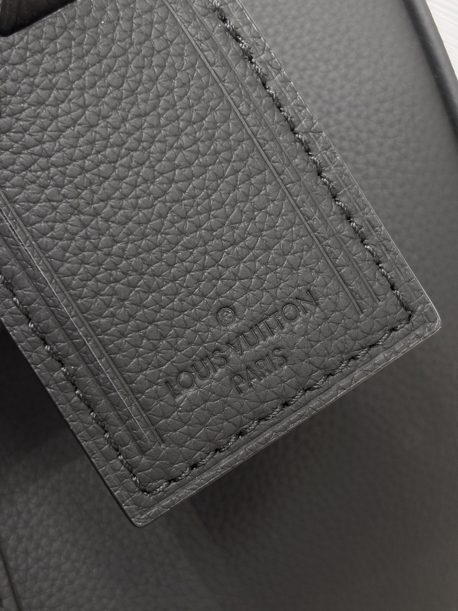 Louis Vuitton leather tag and stitched pocket close-up, dark gray.
