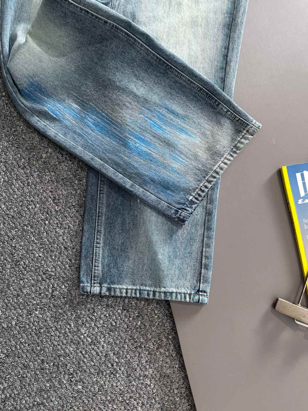 Folded light blue denim jeans with washed blue pattern on the knee area, straight leg