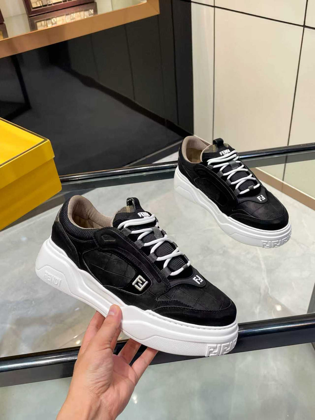 Black lace-up sneakers held in hand, white chunky sole with Fendi logos