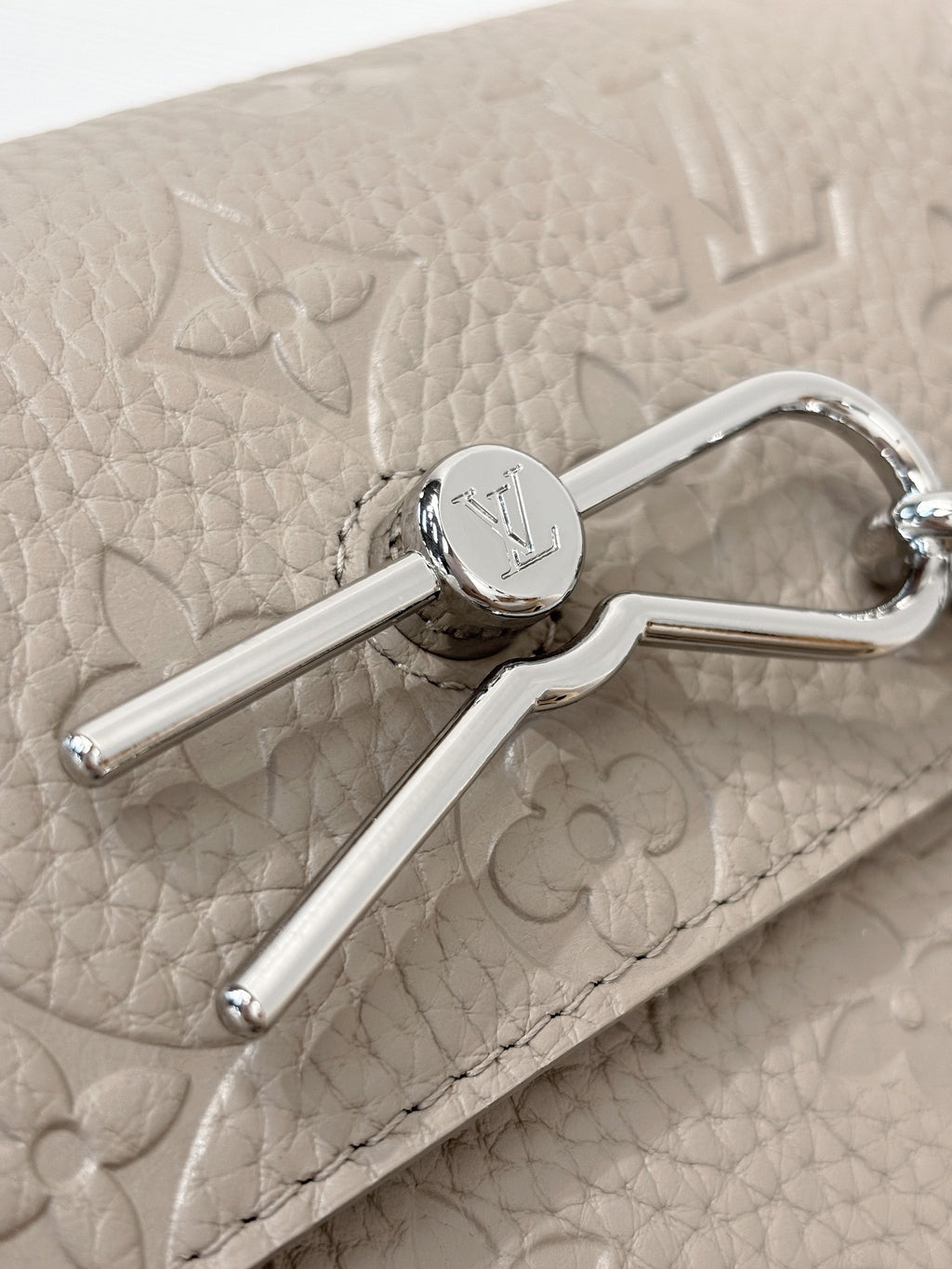 Close-up of light gray bag flap and silver clasp with engraved circular emblem