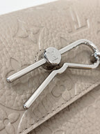 Close-up of light gray bag flap and silver clasp with engraved circular emblem
