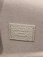 Close-up of light gray leather tag with “Louis Vuitton” text stitched on bag