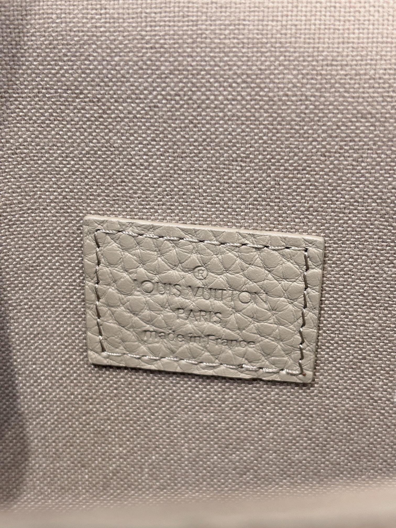Close-up of light gray leather tag with “Louis Vuitton” text stitched on bag