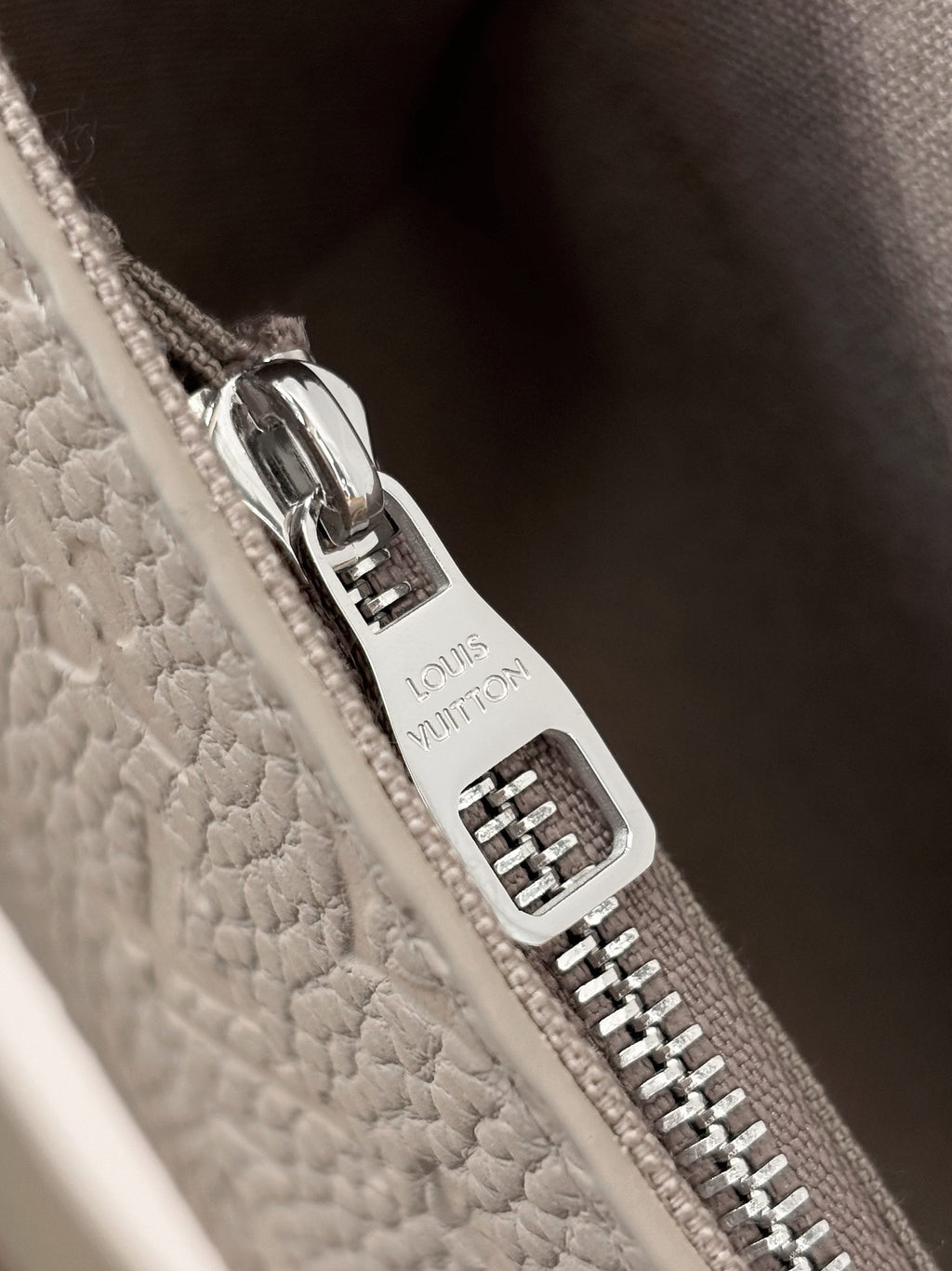 Close-up of silver zipper pull and “Louis Vuitton” hardware on light gray bag