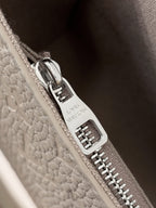 Close-up of silver zipper pull and “Louis Vuitton” hardware on light gray bag