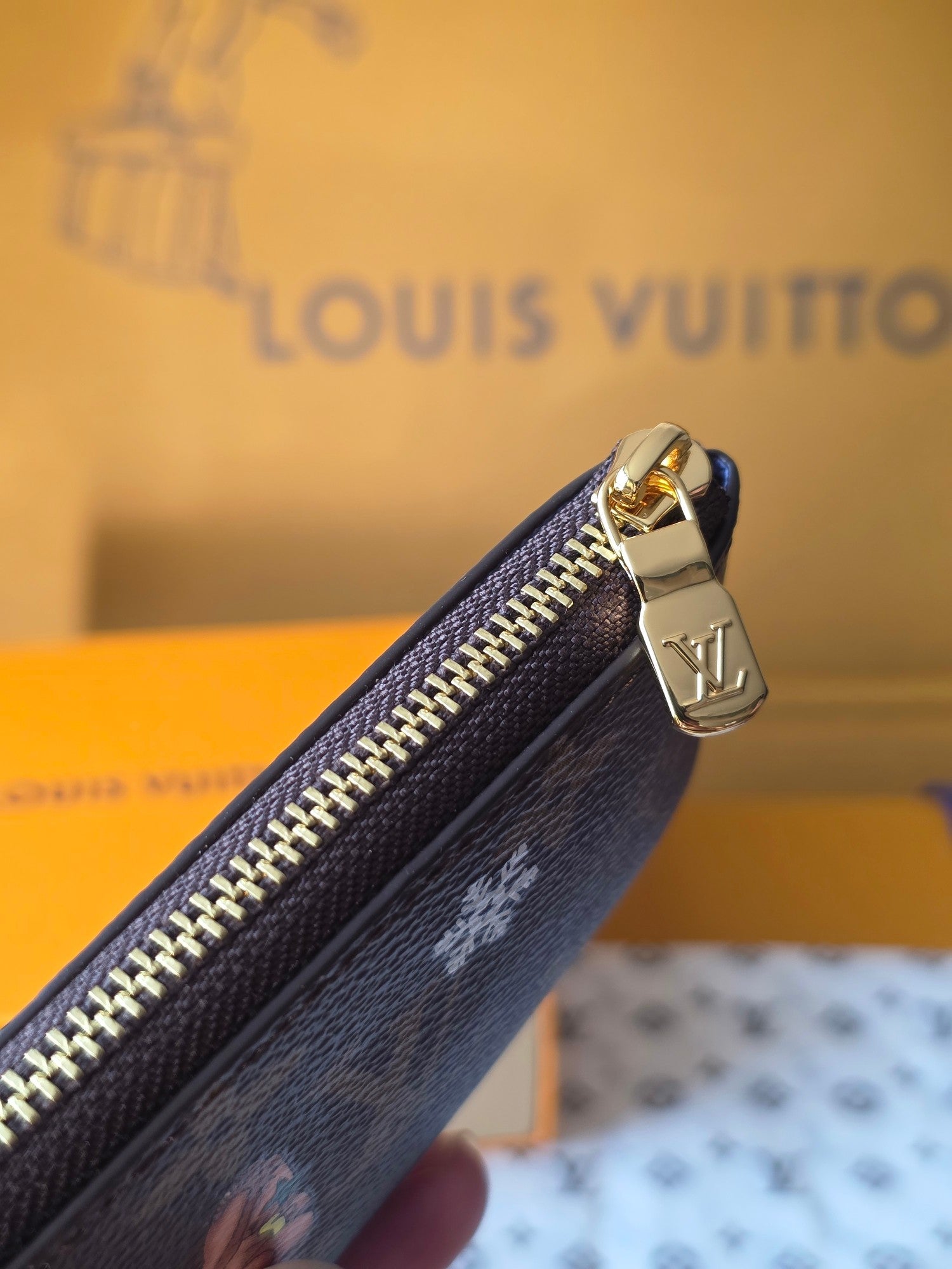 Louis Vuitton small bag zipper edge close-up with gold hardware and brown leather.