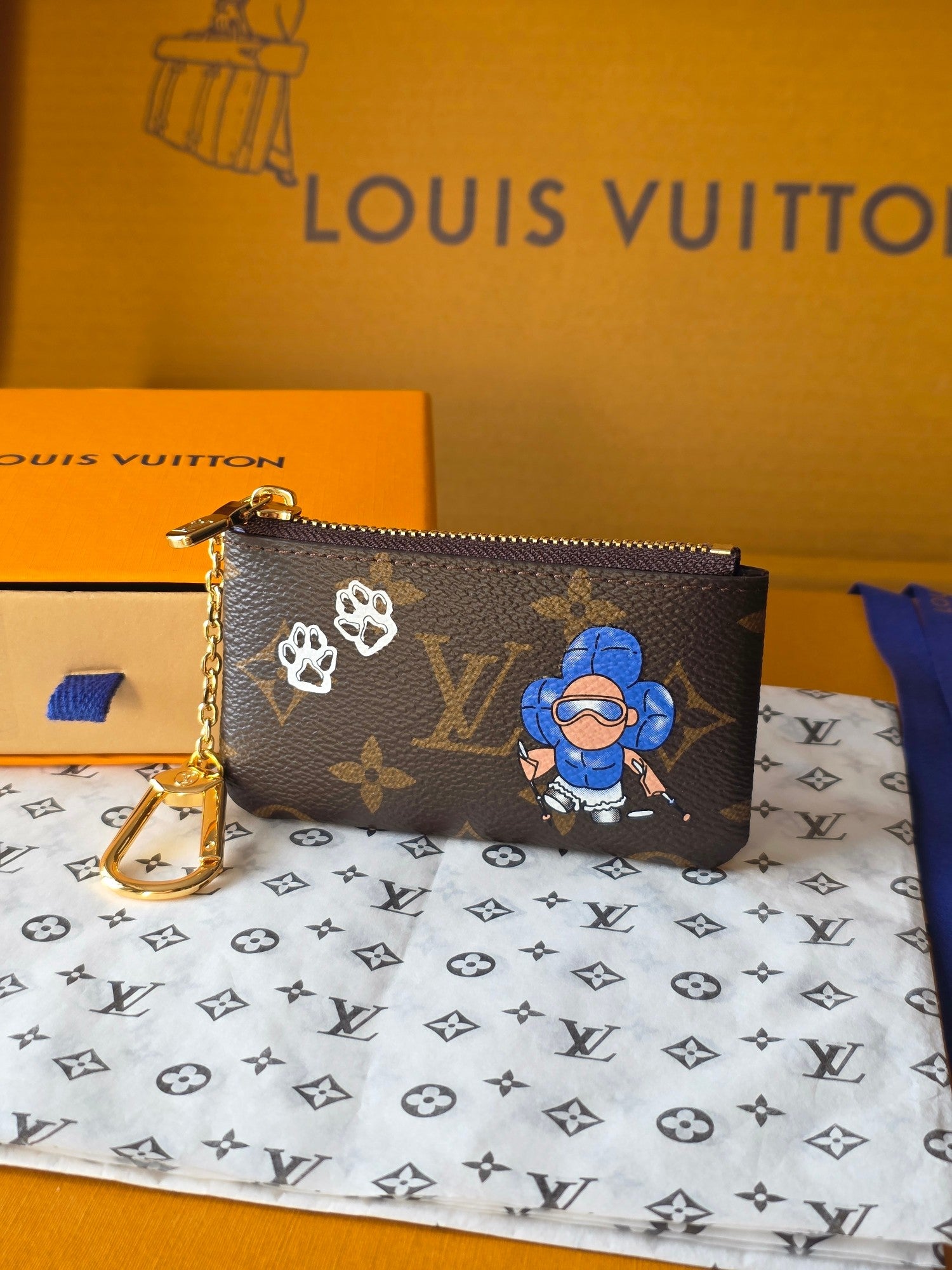 Louis Vuitton small bag with zip top, monogram print and blue character artwork.