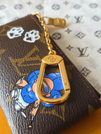 Louis Vuitton small bag with gold chain and blue cartoon charm accessory.