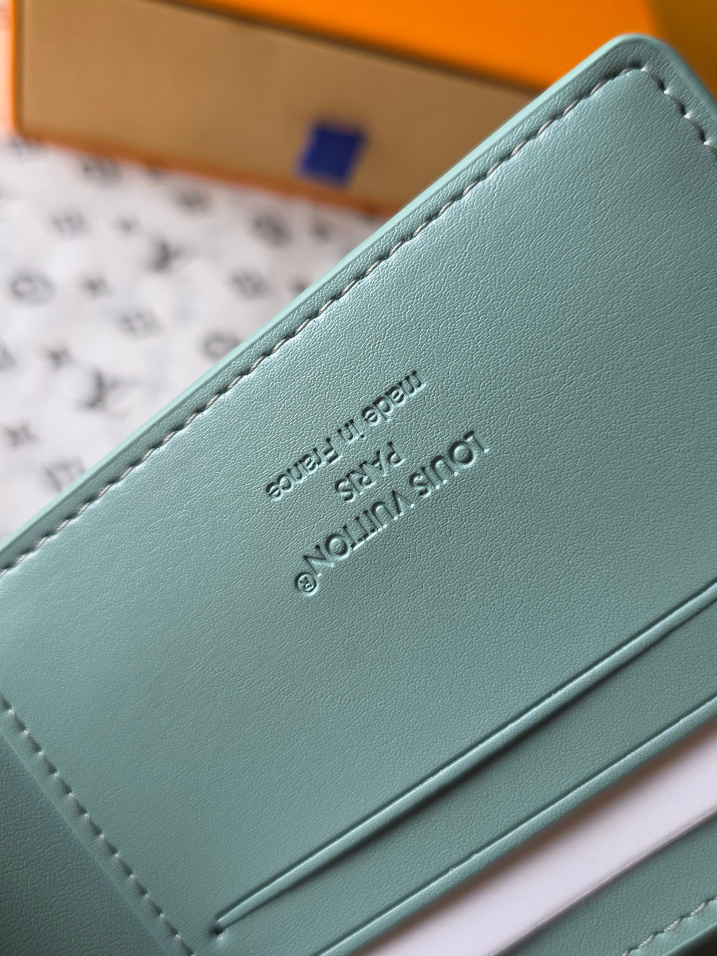 Light blue small bag wallet close-up of embossed Louis Vuitton text