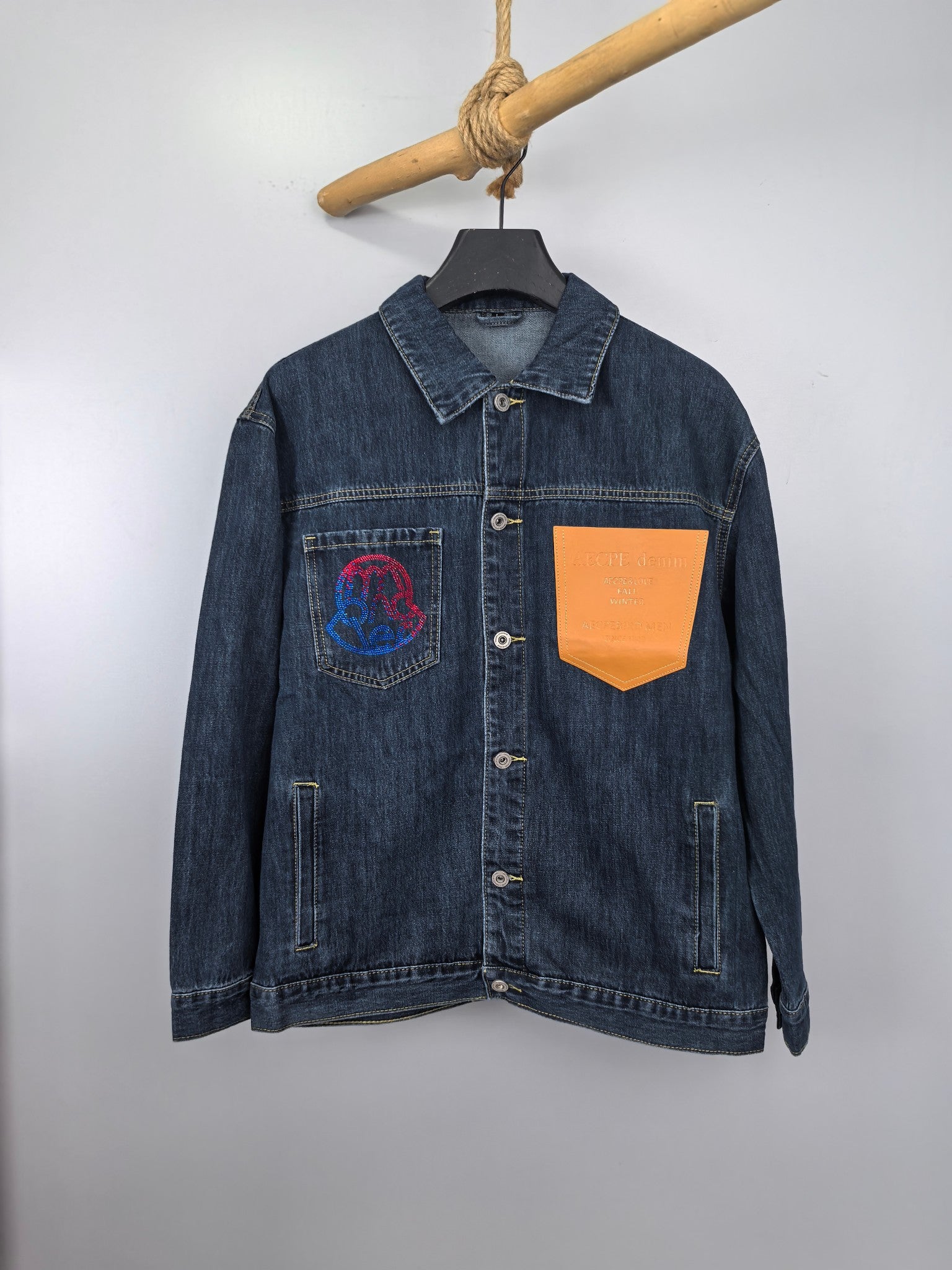Blue denim jacket with button front, point collar, and chest graphic patch