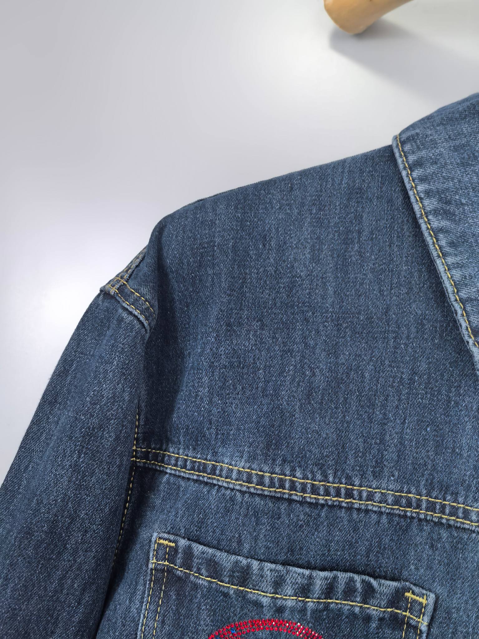 Blue denim jacket shoulder and chest pocket close-up with contrast stitching