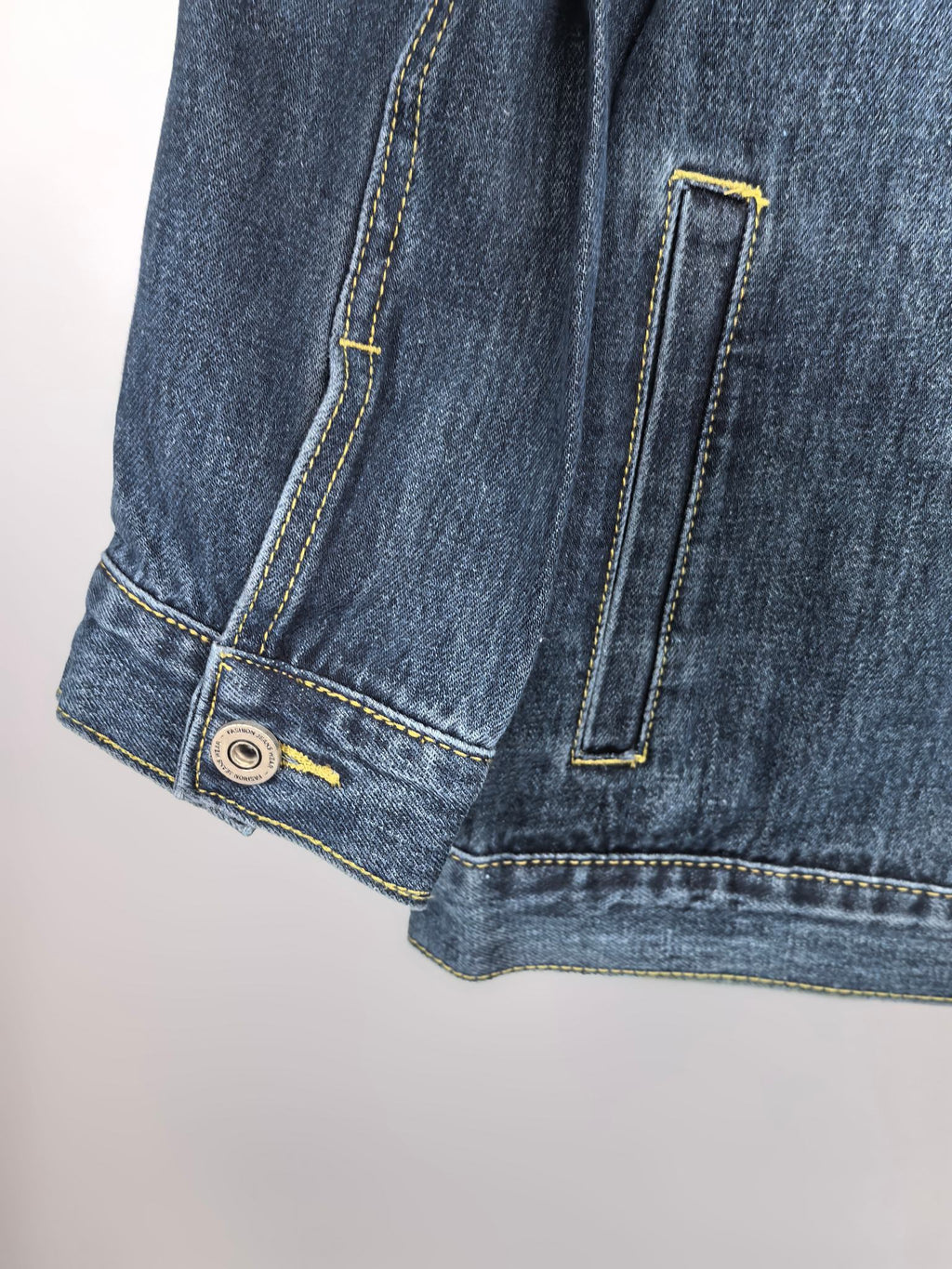 Blue denim jacket lower hem close-up with side pocket and strap detail
