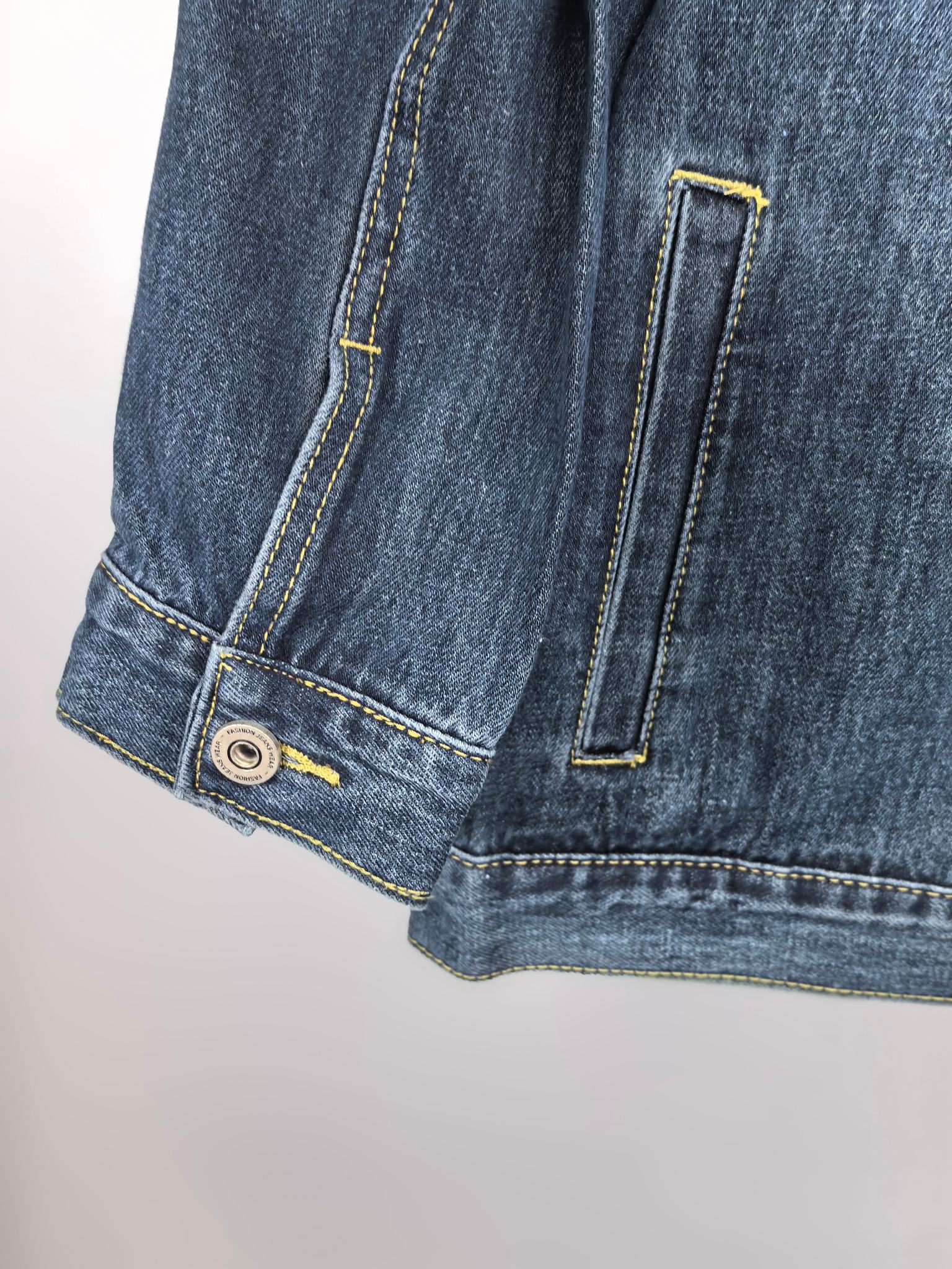 Blue denim jacket lower hem close-up with side pocket and strap detail