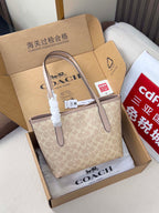Beige COACH monogram tote bag with leather strap detail and gift tags in box