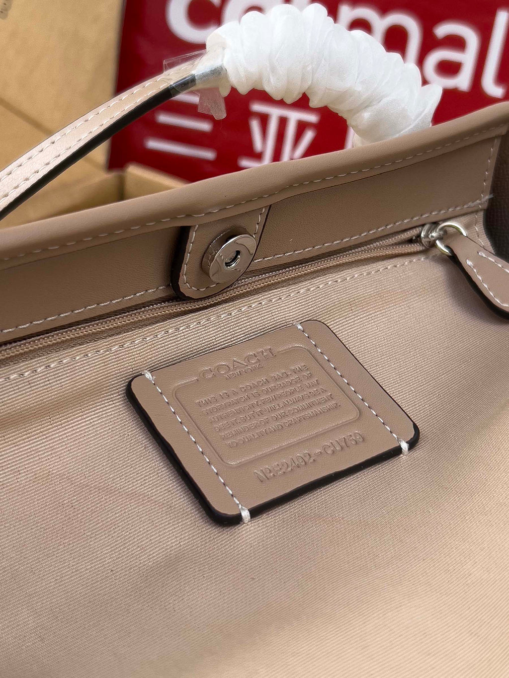 Beige COACH tote bag close-up of zipper pull tab and hanging leather charm
