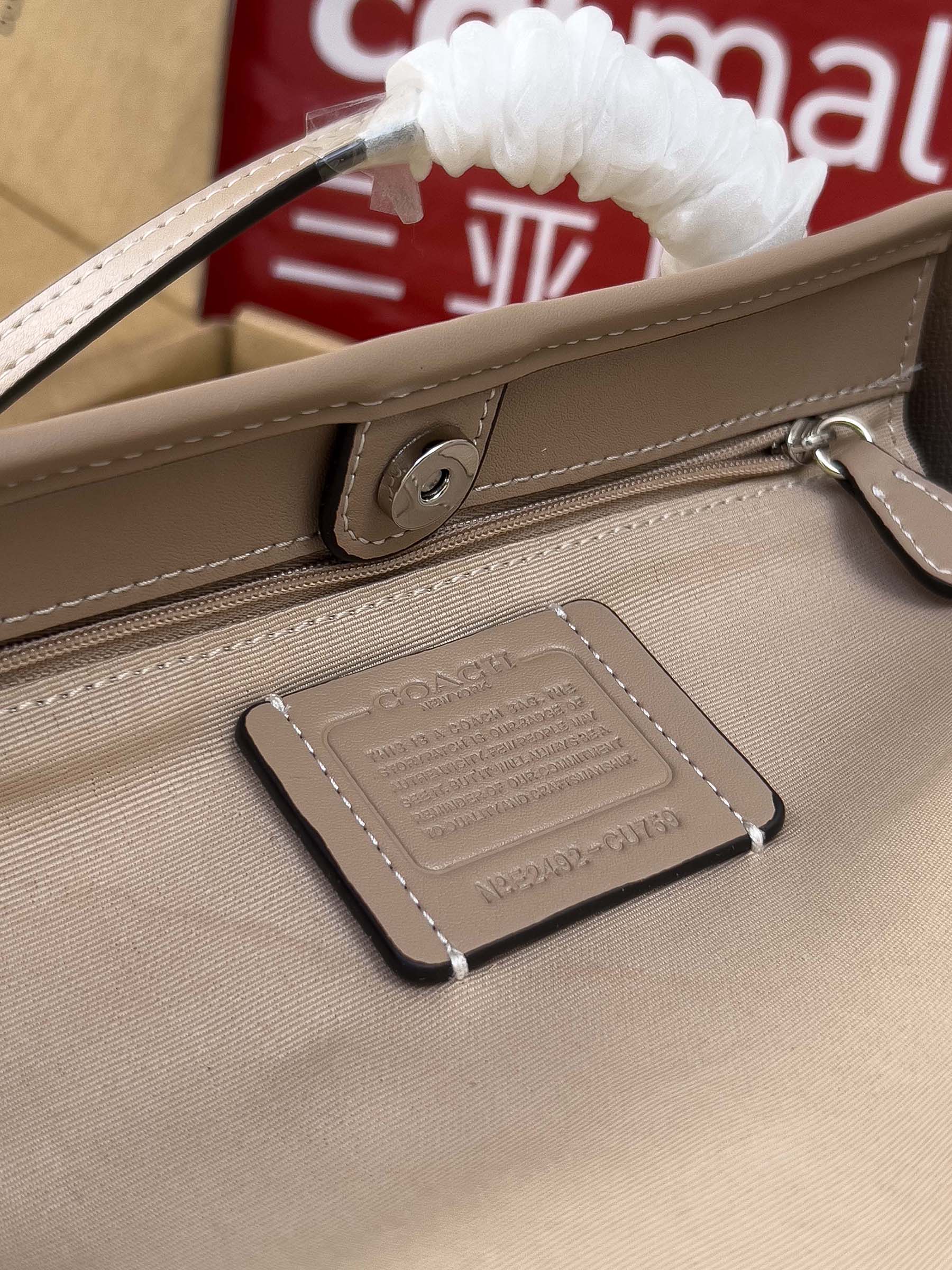 Beige COACH tote bag close-up of zipper pull tab and hanging leather charm
