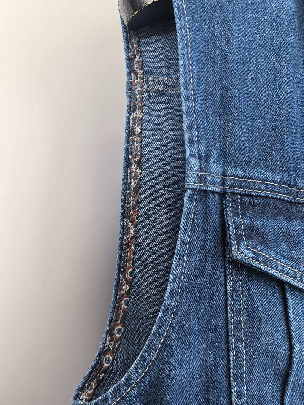 Gucci blue denim vest side seam close-up with buttoned pocket and curved stitching