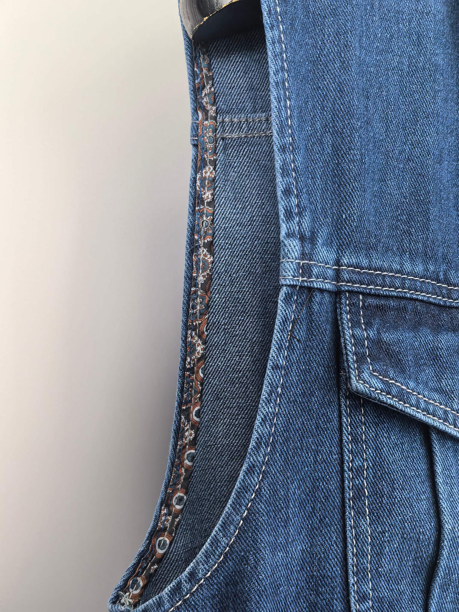 Gucci blue denim vest side seam close-up with buttoned pocket and curved stitching