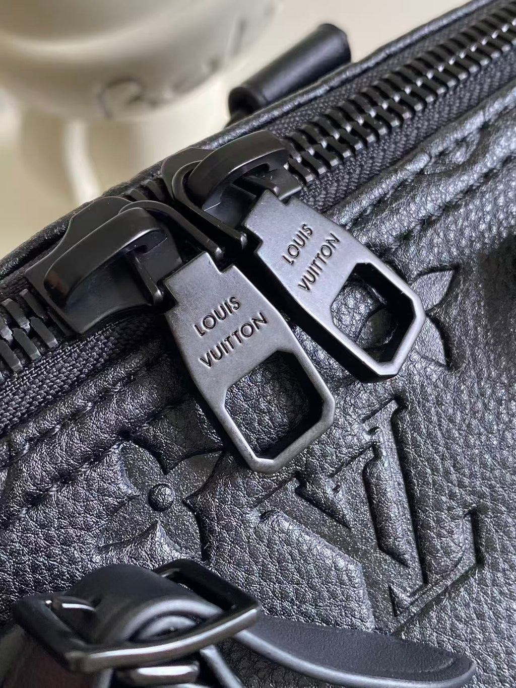 Louis Vuitton zipper pull hardware on dark navy leather bag, close-up