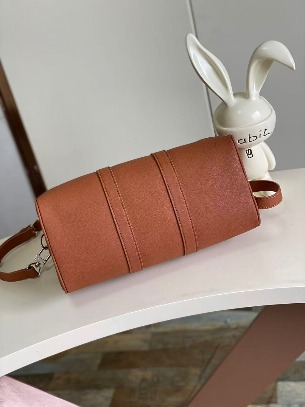 Brown leather cylindrical handbag with top handle and crossbody strap, stitched paneling