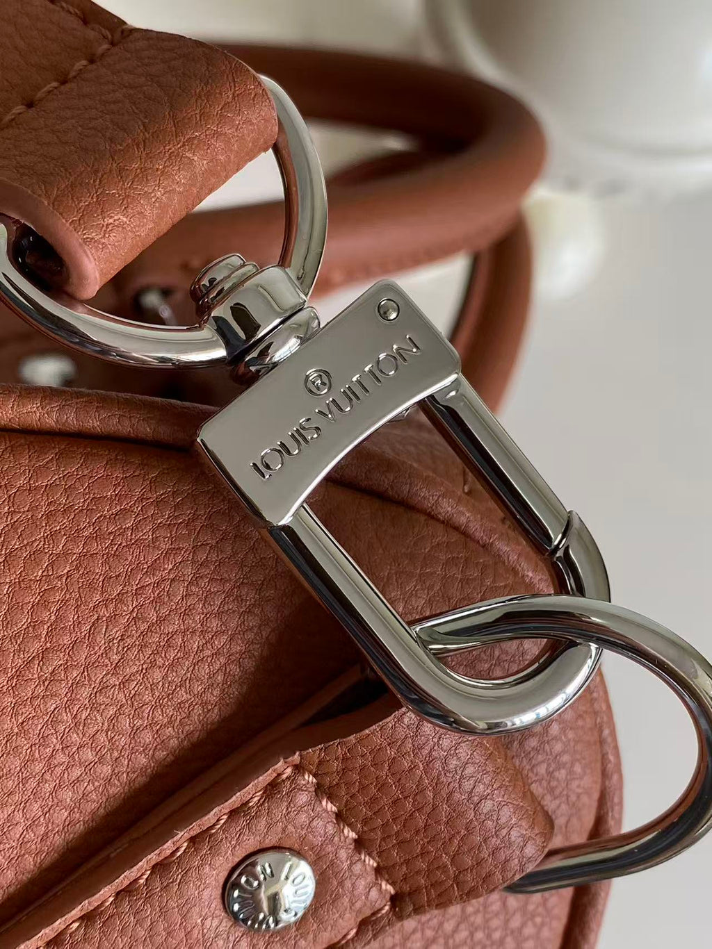 Brown leather bag with silver carabiner clip and D-ring hardware, logo plate