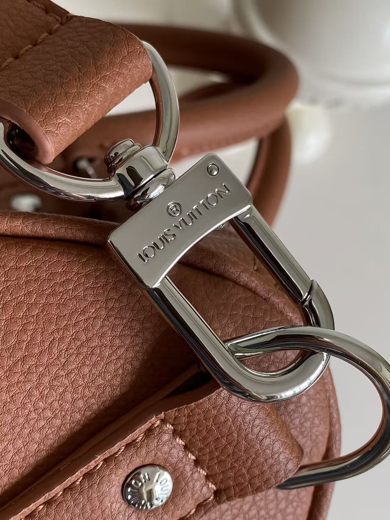 Brown leather bag with silver carabiner clip and D-ring hardware, logo plate
