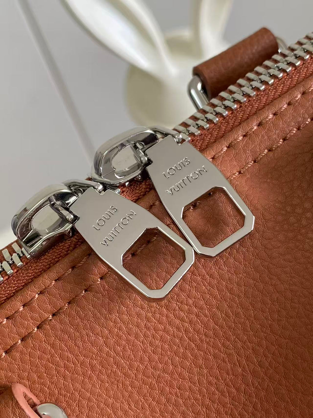 Brown leather bag zipper with silver metal pulls and logo-engraved hardware plates