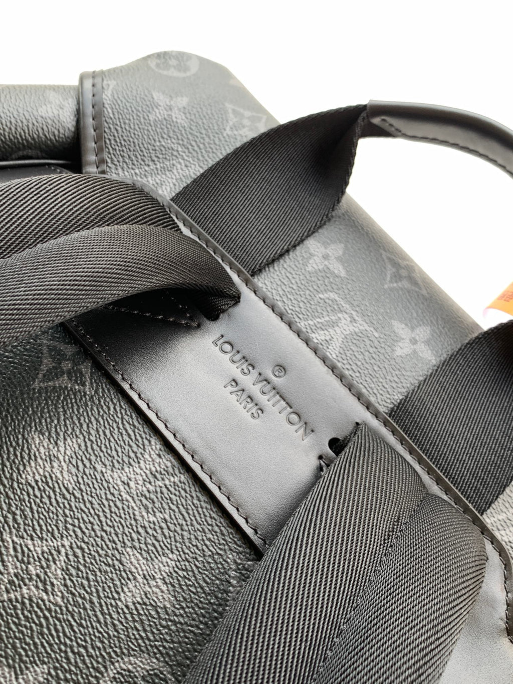 Monogram backpack strap and leather label patch on dark gray fabric