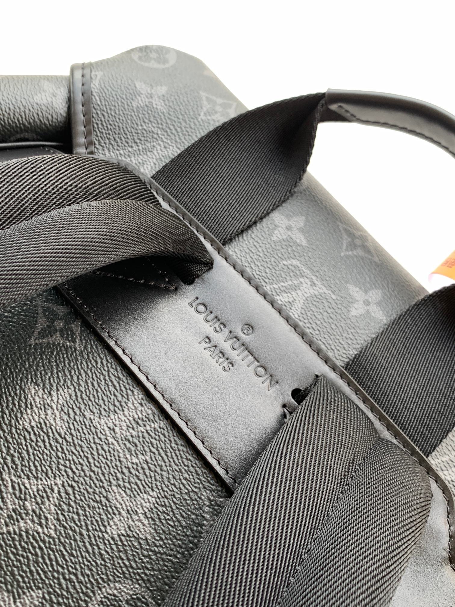 Monogram backpack strap and leather label patch on dark gray fabric