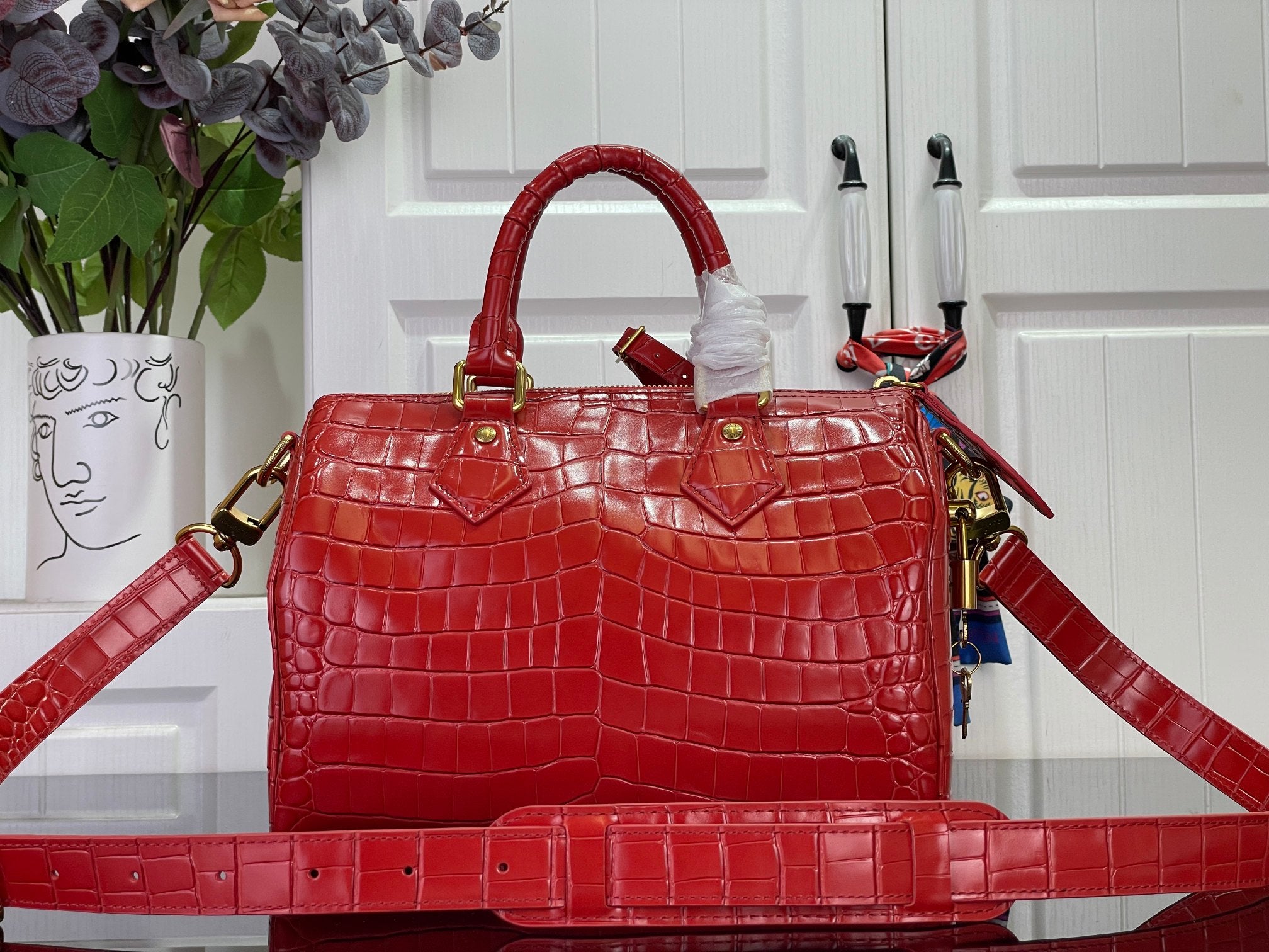 Louis Vuitton red structured tote bag with top handles, gold hardware, and long strap