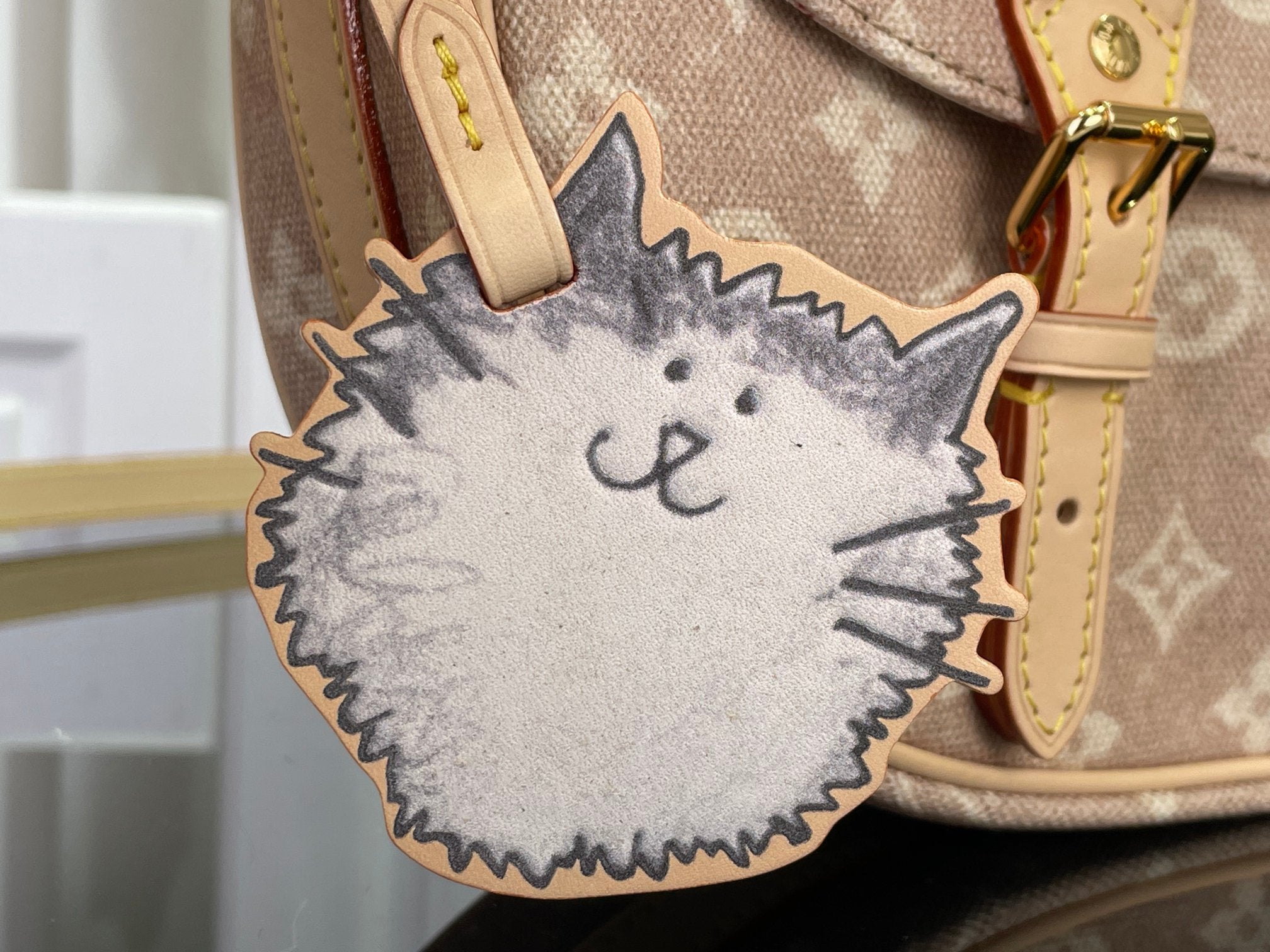 Louis Vuitton cat-shaped charm on bag with tan leather strap and monogram fabric