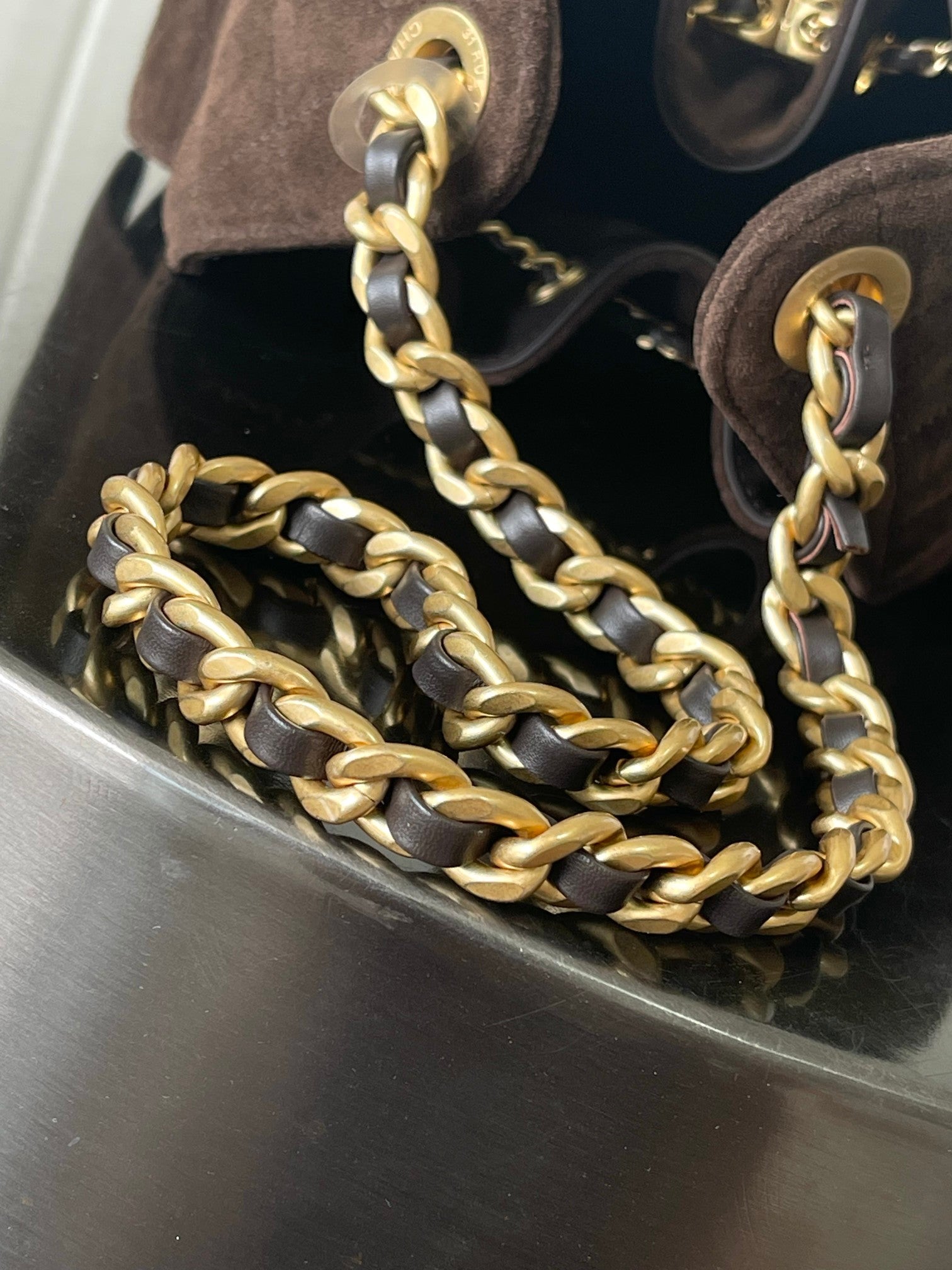 Chanel bag chain strap close-up with gold links over dark brown fabric