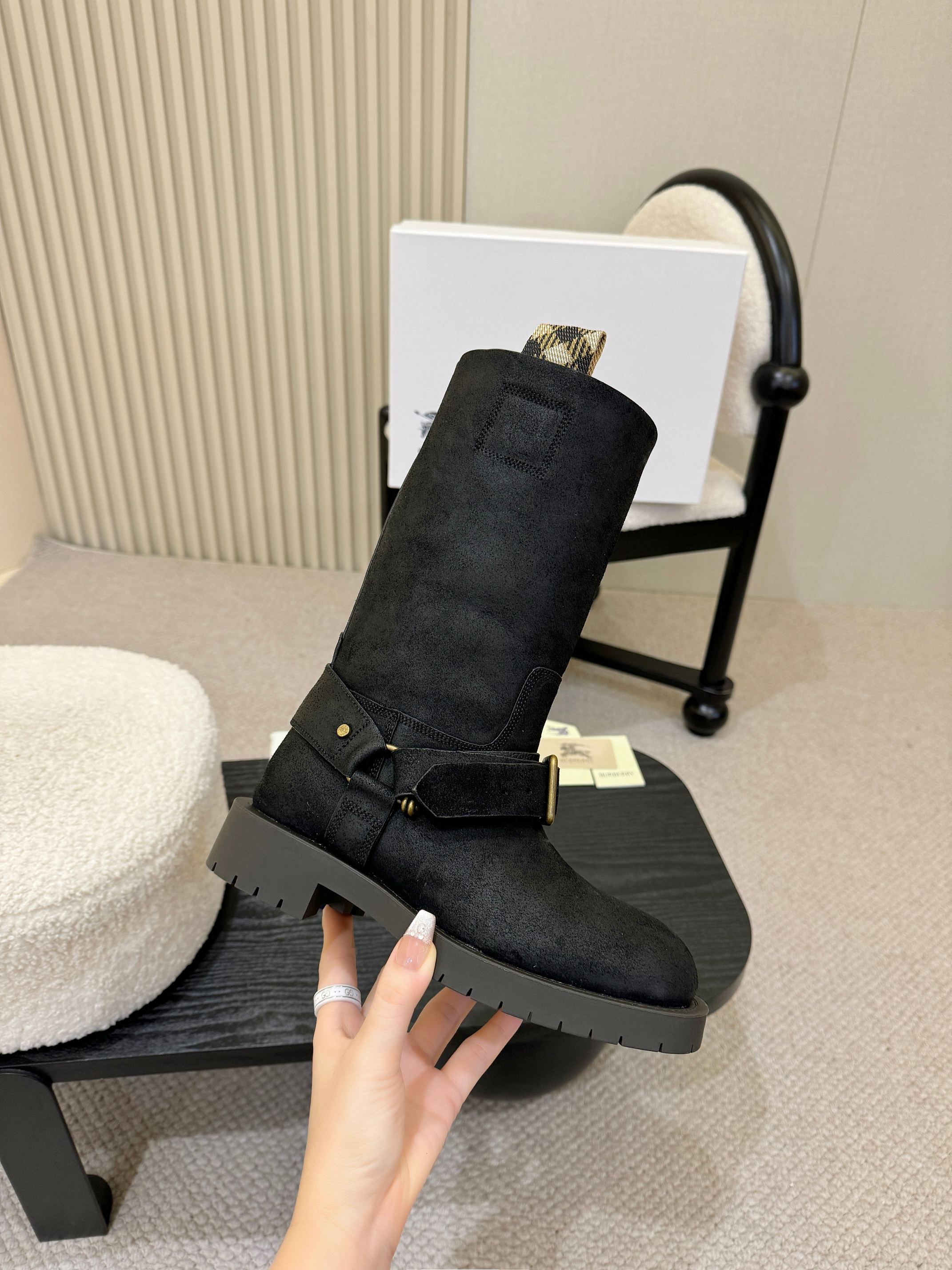 Black mid-calf boot with gold buckle strap, held in hand