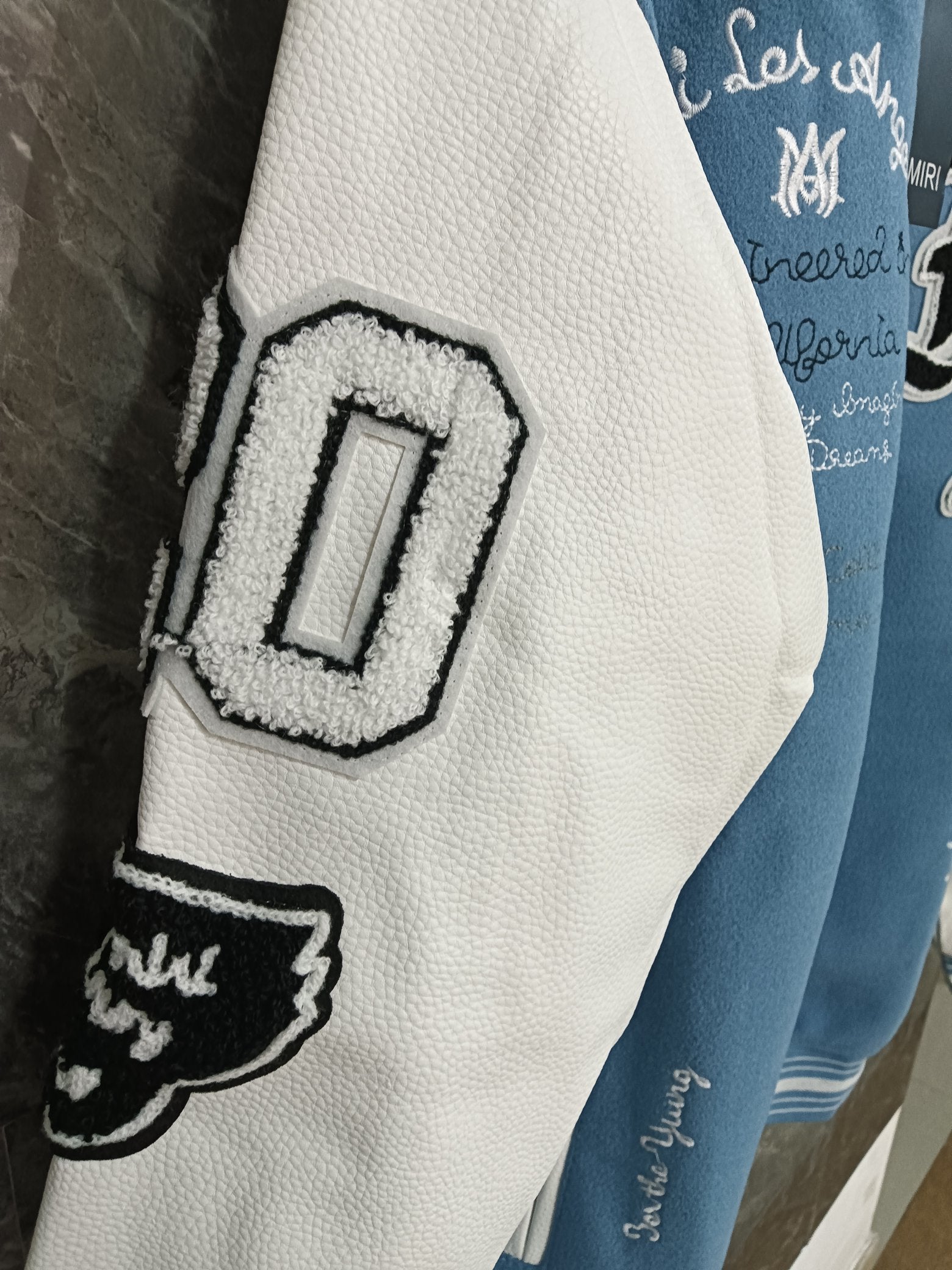 White leather-look sleeve panel with black embroidered letter patch on varsity jacket