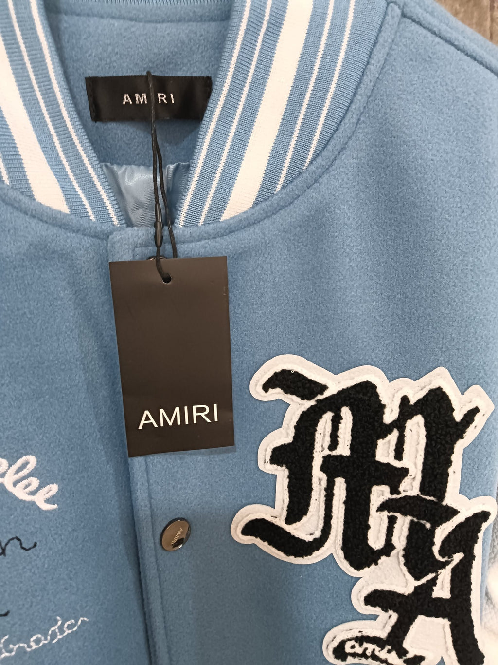 Light blue varsity jacket front with ribbed collar and large embroidered logo patch