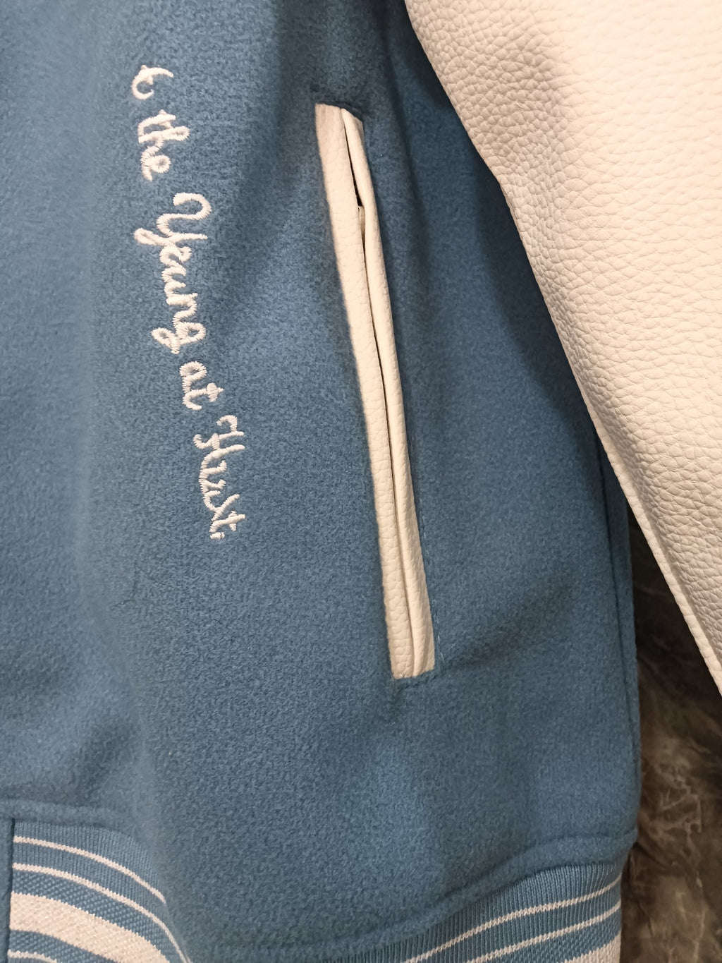 Sleeve side of light blue varsity jacket with embroidered script and striped rib cuff