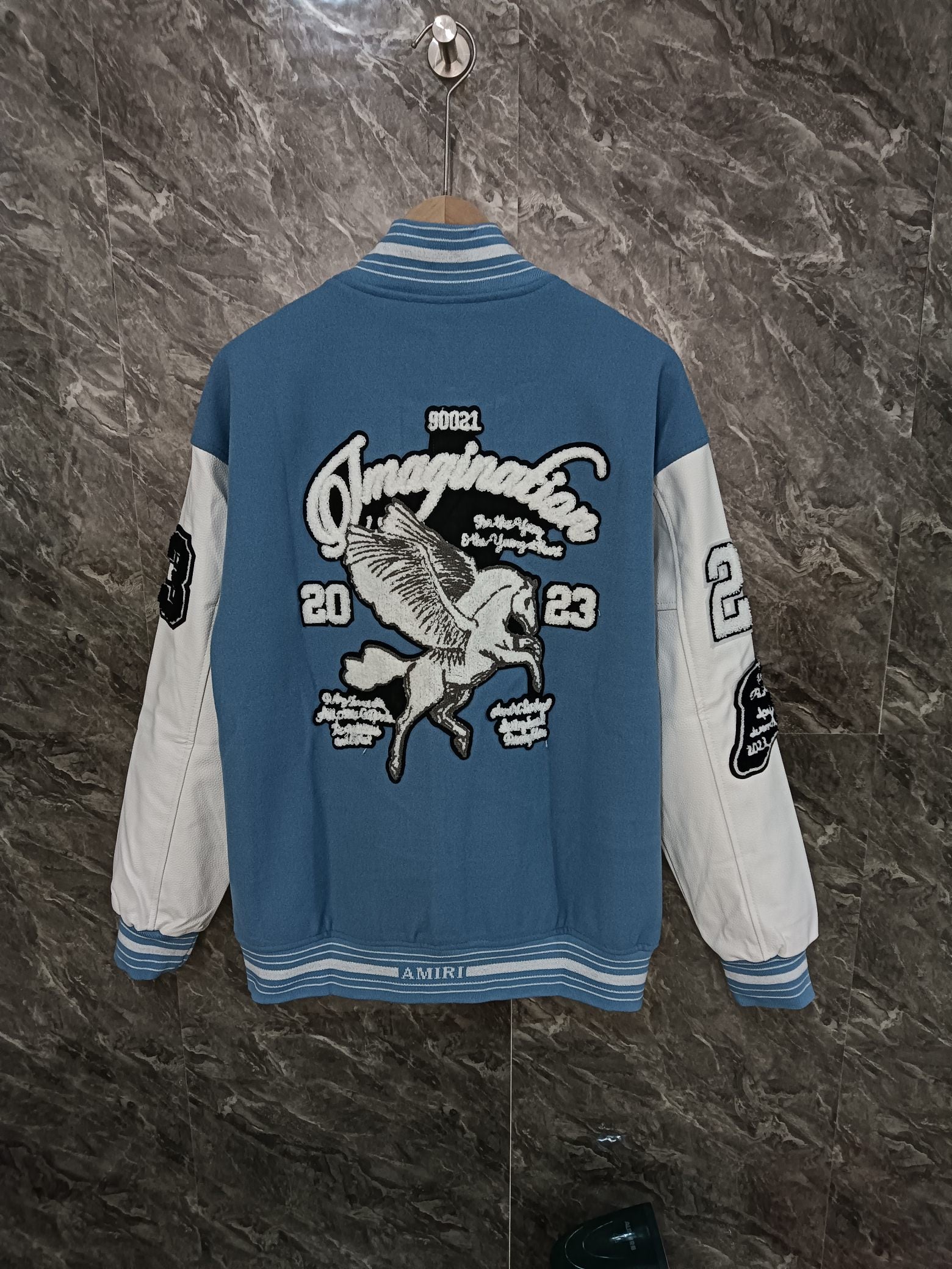 Back view of blue varsity jacket with large embroidered graphic and striped hem